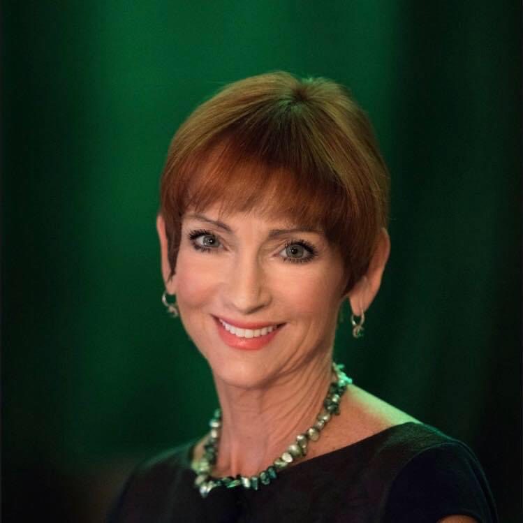 Headshot of Beth Klein with a fiery red pixie haircut in front of a signature green background.