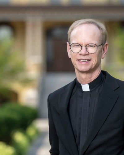 priest with glasses standing and smiling warmly on Notre Dame campus