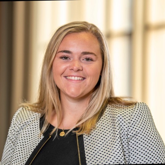 blonde woman wearing black blouse and gray blazer smiling