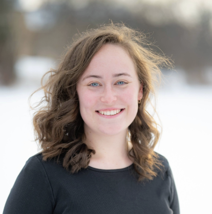 brunette with short, curly hair smiling in front of a snowy terrain